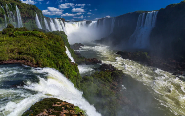 HD PC wallpaper showcasing the stunning Iguazu Falls surrounded by lush greenery under a bright blue sky, capturing the power and beauty of nature.