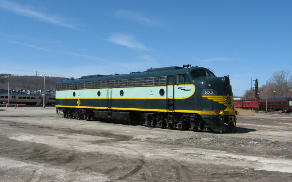 HD PC desktop wallpaper background of a teal-and-yellow diesel locomotive train vehicle parked in a rail yard under a clear blue sky.