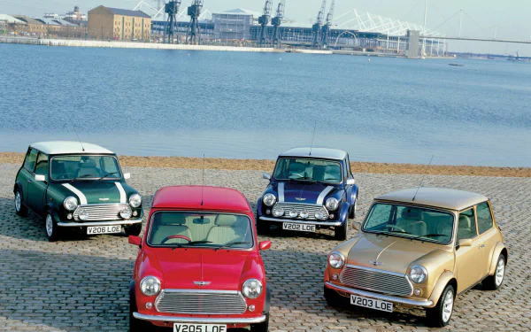 HD PC desktop wallpaper featuring four classic Mini Cooper vehicles in different colors parked by a waterfront with an industrial skyline in the background.