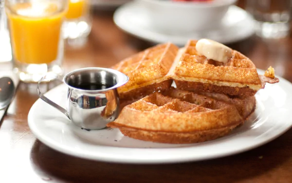 HD PC desktop wallpaper featuring a close-up of golden waffles served with a pat of butter and syrup on a white plate, accompanied by a glass of orange juice.