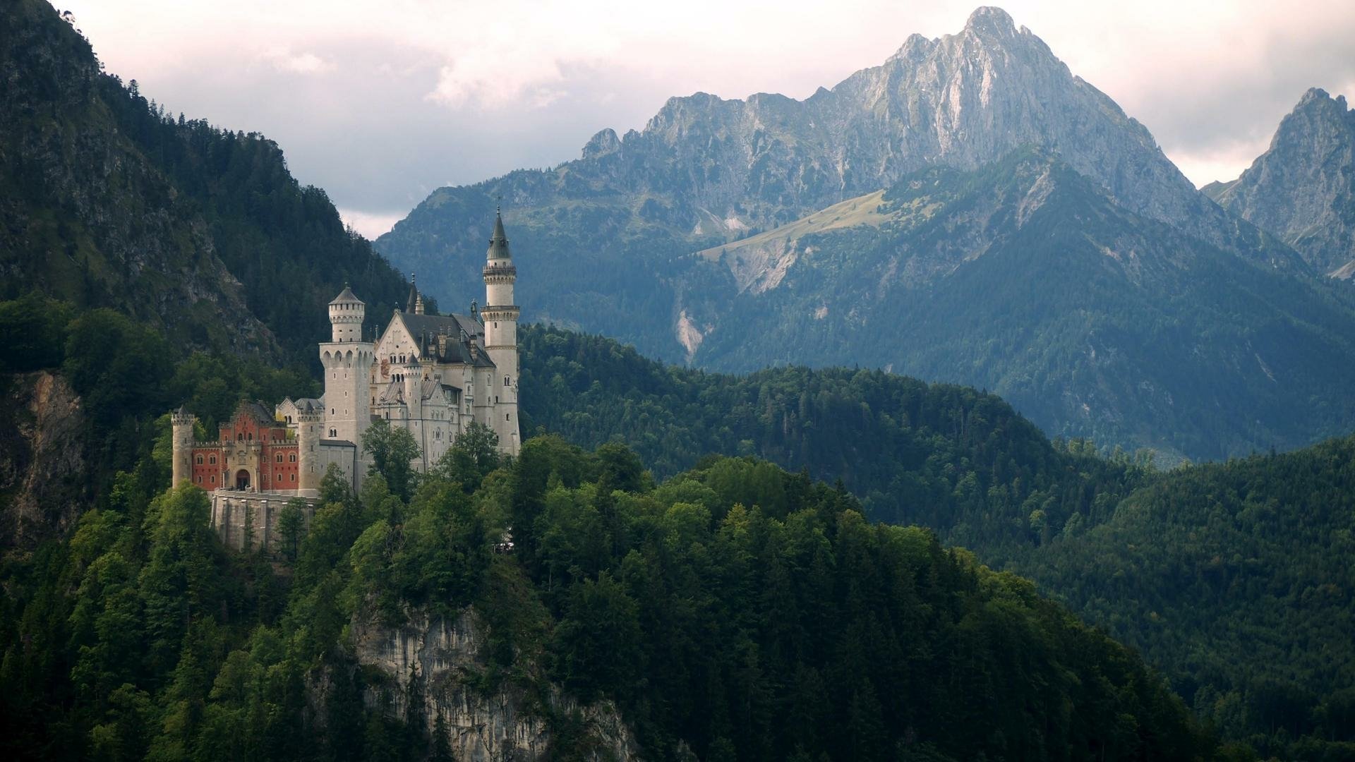 Neuschwanstein Castle, a man-made fairy-tale fortress on a forested Bavarian ridge with the Alps behind — HD PC desktop wallpaper and background.