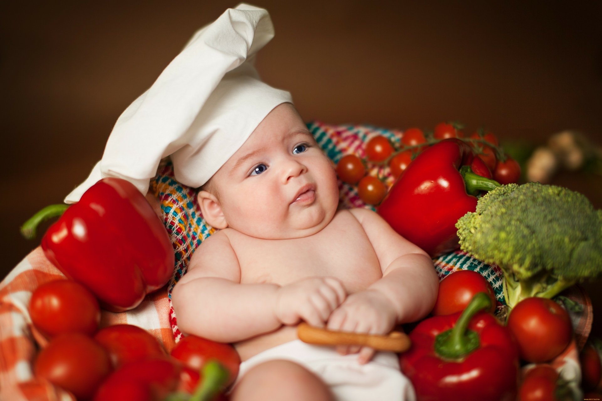 A baby wearing a chef’s hat surrounded by fresh vegetables, captured in vibrant detail for a 4K Ultra HD PC desktop wallpaper.
