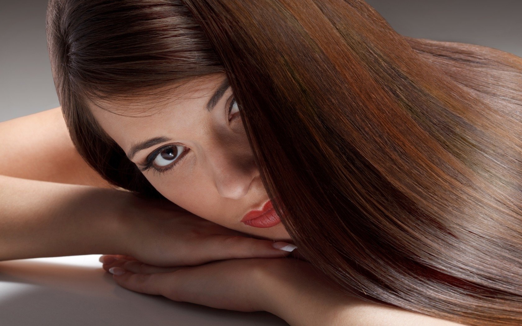 A close-up of a woman with long, glossy hair, resting her head on her arms. The image serves as a striking HD desktop wallpaper and background, highlighting her captivating gaze.