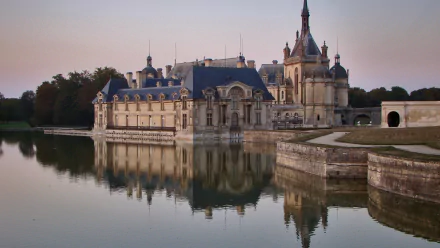HD desktop wallpaper showcasing the man-made Château de Chantilly reflected in calm waters under a soft evening sky.