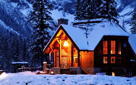 HD desktop wallpaper of a cozy house illuminated by warm lights, nestled in a snowy mountain landscape during twilight.