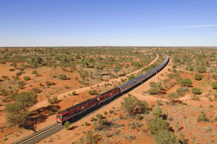A 4K Ultra HD wallpaper of The Ghan train winding through the arid Australian outback under a clear blue sky.