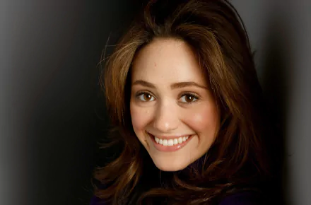 HD desktop wallpaper featuring a close-up portrait of celebrity Emmy Rossum smiling against a dark background.