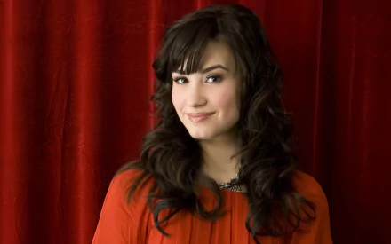 Demi Lovato smiles in front of a rich red backdrop, showcasing her vibrant style. This high-definition image serves as a striking desktop wallpaper for music fans.