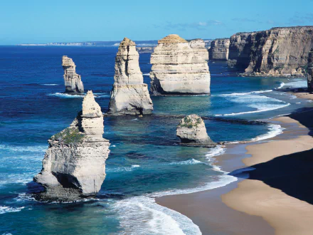 HD desktop wallpaper showcasing the natural limestone rock formations of The Twelve Apostles along a rugged coastline under a clear blue sky.