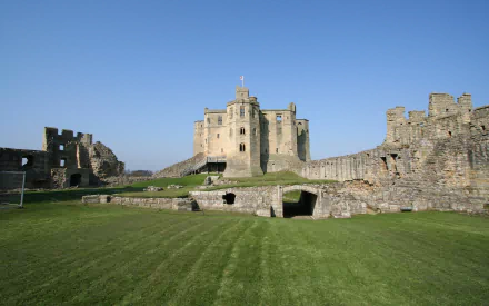 A stunning HD wallpaper featuring Warkworth Castle, showcasing its towering architecture and lush green grounds under a clear blue sky.