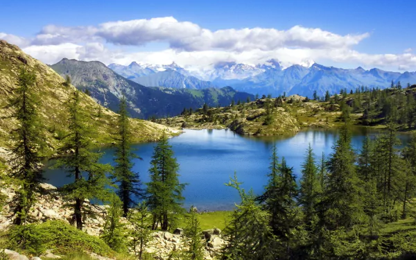 A serene lake surrounded by lush greenery and majestic mountains under a blue sky, capturing the beauty of nature in this stunning HD desktop wallpaper.