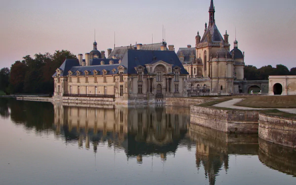 HD desktop wallpaper showcasing the man-made Château de Chantilly reflected in calm waters under a soft evening sky.