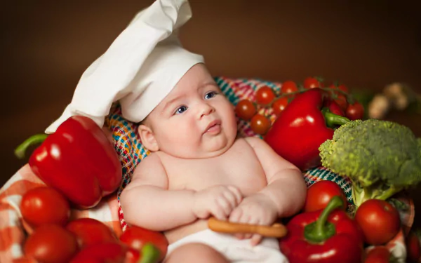 A baby wearing a chef’s hat surrounded by fresh vegetables, captured in vibrant detail for a 4K Ultra HD PC desktop wallpaper.