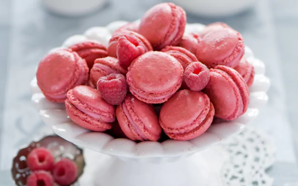 HD desktop wallpaper featuring a close-up of vibrant pink macarons garnished with fresh raspberries on a white cake stand.