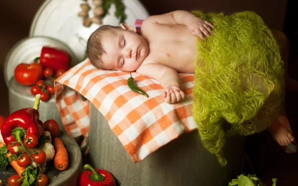 A peaceful baby sleeps on a checkered pillow surrounded by fresh vegetables, captured in a vibrant 4K Ultra HD photography wallpaper.