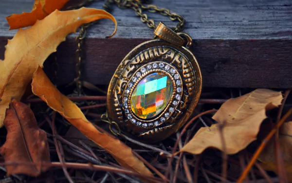 A close-up of an ornate brass locket with a colorful gemstone, resting on rustic wooden surfaces and surrounded by autumn leaves. A beautiful 4K Ultra HD desktop wallpaper and background.