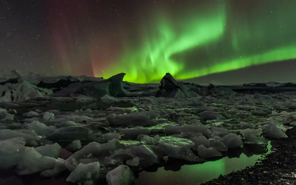 A stunning display of the aurora borealis illuminates the night sky, casting a green glow over icy terrain, creating a breathtaking nature scene for an HD desktop wallpaper.