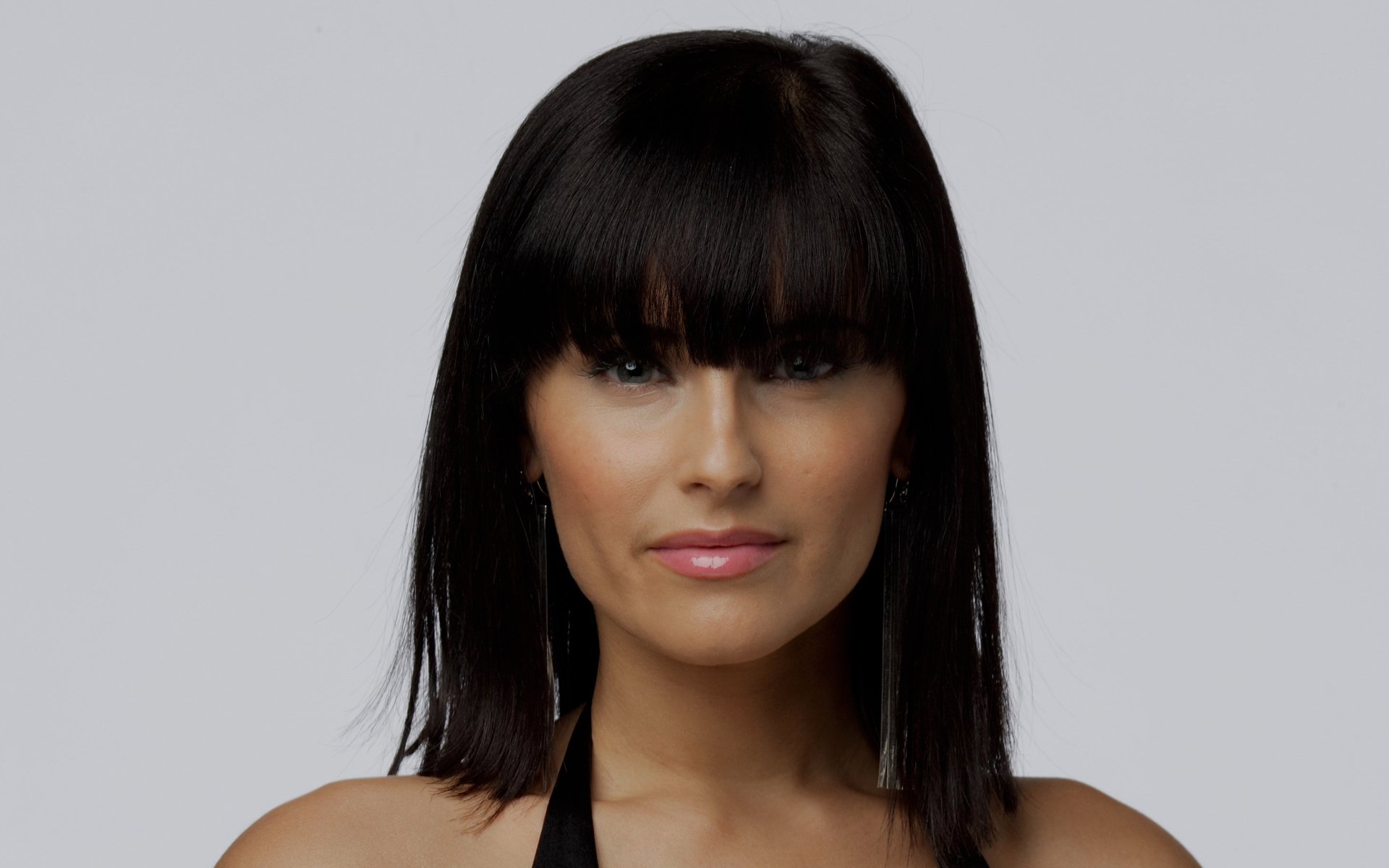 Close-up HD desktop wallpaper of Nelly Furtado with straight black hair and bangs, showcasing her music career with a neutral gray background.