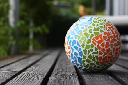 A colorful mosaic ball on wooden planks with a blurred green background, captured in sharp detail for a 4K Ultra HD photography PC desktop wallpaper.