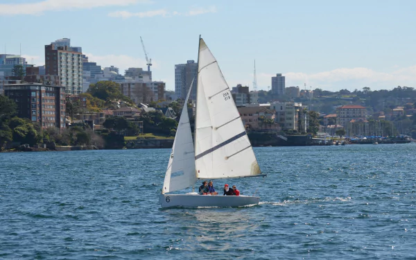 A sailboat with white sails glides across blue water near a city skyline, captured in HD for a vibrant yacht and sailing-themed desktop wallpaper.