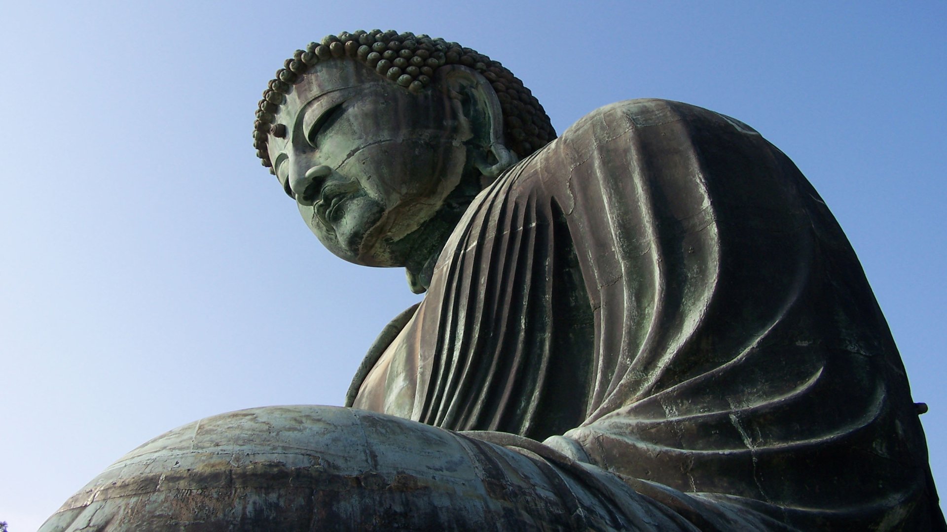 Close-up of a religious Buddha statue gazing downward against a clear sky — 2K Quad HD PC desktop wallpaper and background.