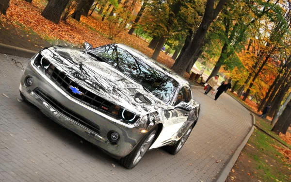 A sleek Chevrolet Camaro parked along a tree-lined path, surrounded by autumn foliage. This HD desktop wallpaper captures the car's modern design and vibrant seasonal setting.