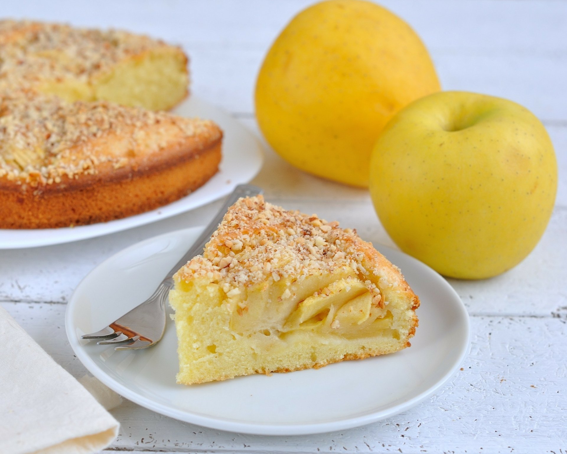 A slice of pie on a white plate, topped with crumbled nuts, alongside whole yellow apples. This high-definition image serves as a vibrant desktop wallpaper.