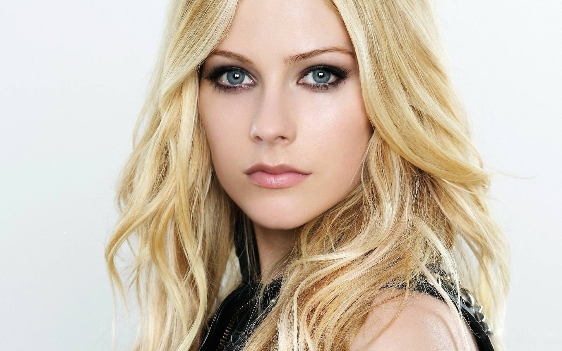 Avril Lavigne poses confidently with flowing blonde hair and striking eyes, featured as a vibrant HD PC desktop wallpaper celebrating her music career.