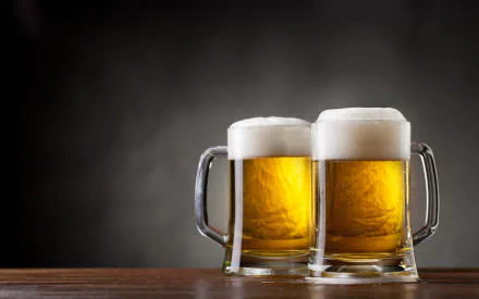 HD PC desktop wallpaper featuring two frothy mugs of golden beer on a wooden surface against a dark background, highlighting food and beer themes.