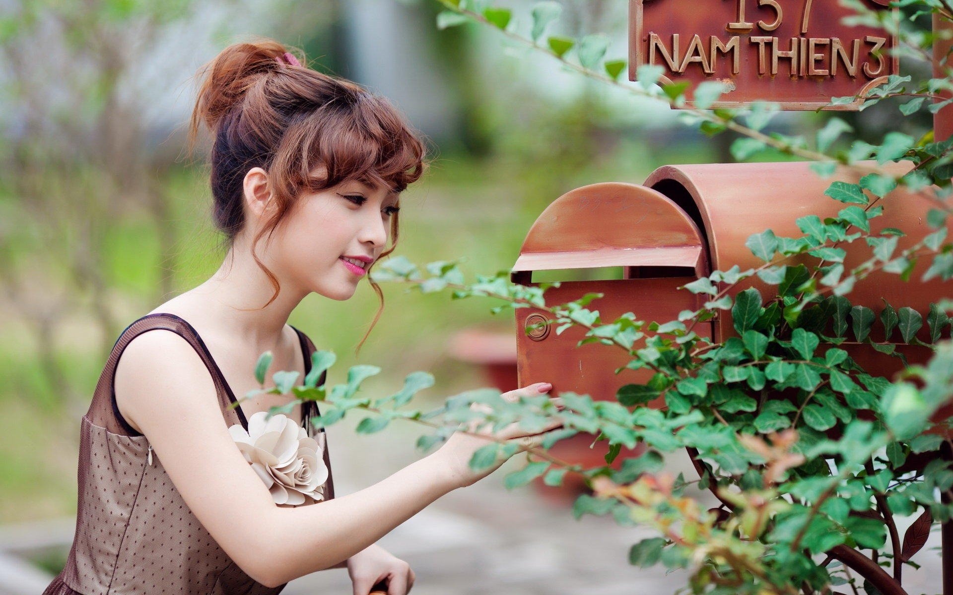 An Asian woman reaching for a mailbox in a serene, greenery-filled setting. HD desktop wallpaper and background.