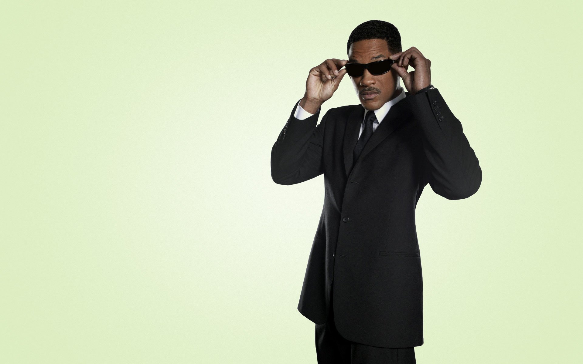 HD PC desktop wallpaper featuring celebrity Will Smith in a black suit adjusting his sunglasses against a light green background.
