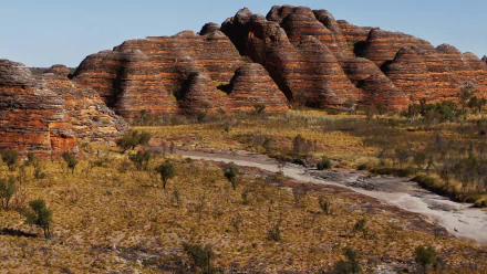 HD PC desktop wallpaper/background: The Kimberley's layered sandstone domes and dry creekbed amid scrubby grasses, showcasing rugged Australian nature.
