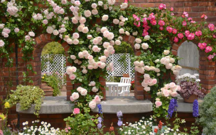 A vibrant rose bush adorned with pink and white flowers climbs a brick wall, framing peaceful garden seating and surrounding colorful blooms, creating a serene man-made floral paradise.