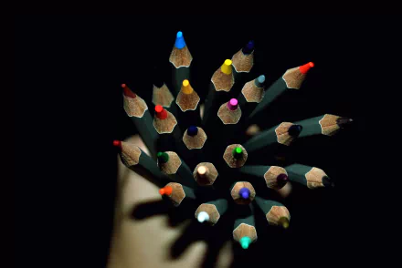 A high-definition photograph featuring a vibrant array of colored pencils arranged in a circular pattern against a dark background, creating an artistic desktop wallpaper.