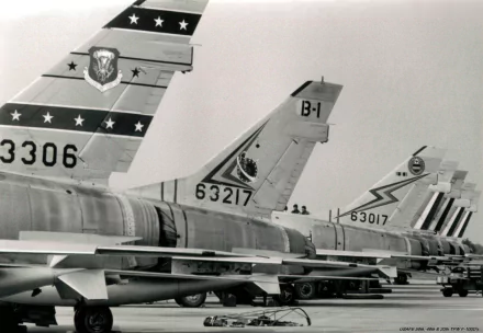 Military 2K Quad HD desktop wallpaper of lined-up North American F-100 Super Sabre tail sections in black-and-white, showing unit markings and serial numbers on an airfield tarmac.