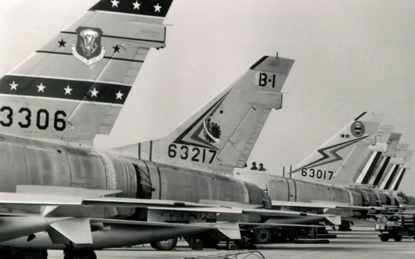 Military 2K Quad HD desktop wallpaper of lined-up North American F-100 Super Sabre tail sections in black-and-white, showing unit markings and serial numbers on an airfield tarmac.