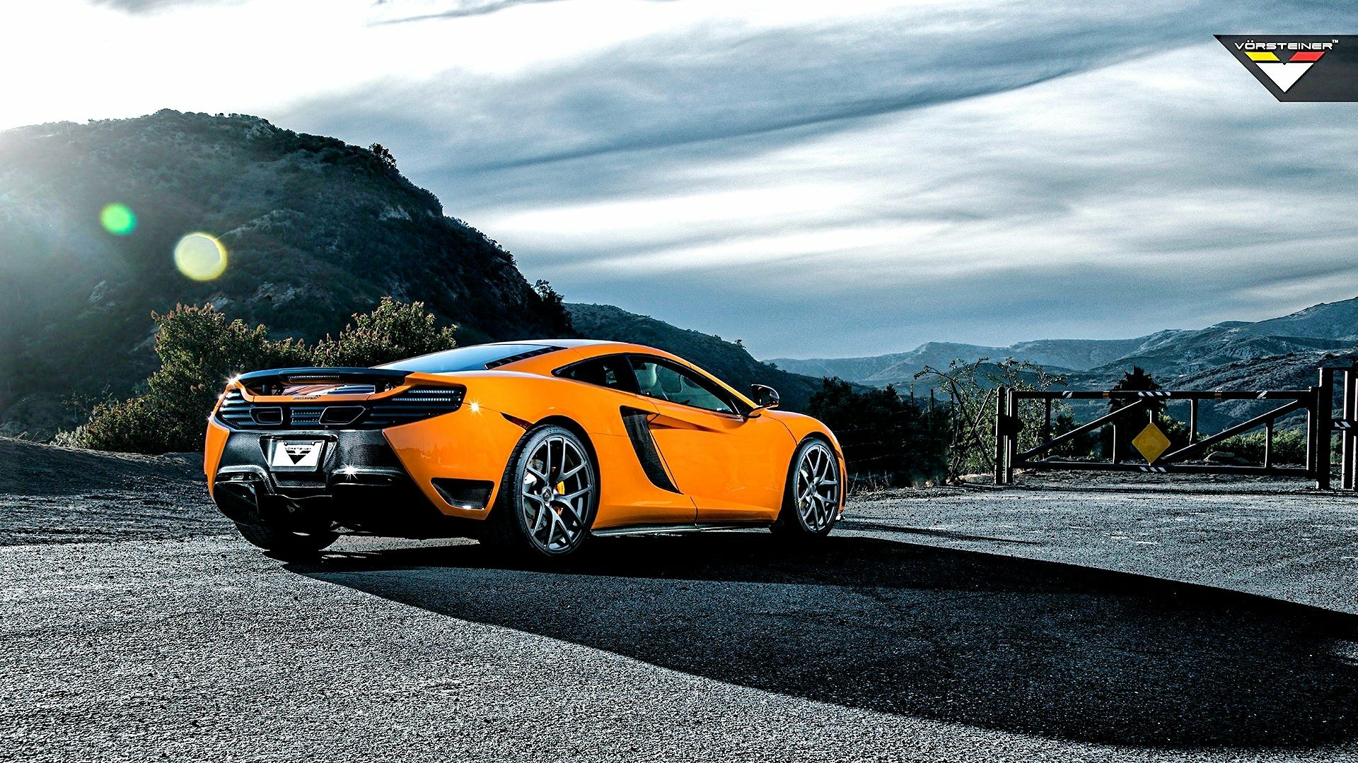 Orange McLaren sports car on a scenic mountain road under a dramatic sky — HD PC desktop wallpaper/background.