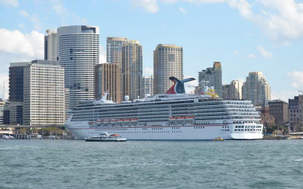 A cruise ship, Carnival Spirit, sails in Sydney Harbour, with the city's skyline towering in the background, showcasing vibrant buildings and a stunning Australian waterfront.