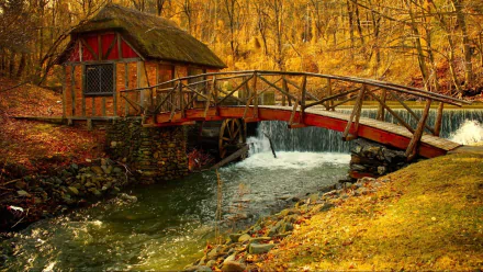 A picturesque watermill nestled by a stream, featuring a charming wooden bridge and surrounded by vibrant autumn foliage. This HD wallpaper captures serene nature and craftsmanship.