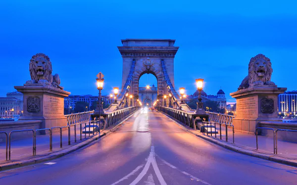 HD desktop wallpaper of Budapest’s iconic Chain Bridge at dusk, featuring its stone lions and illuminated street lamps under a vibrant blue sky in Hungary.