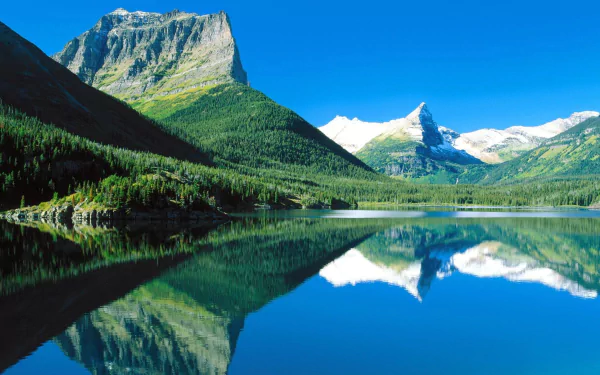 HD PC desktop wallpaper and background: nature scene of snow-capped peaks and green forest mirrored in a clear blue lake, striking reflection.