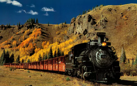 A vintage steam train travels through a picturesque landscape, surrounded by golden autumn foliage and rocky hills, creating a stunning HD wallpaper and background.