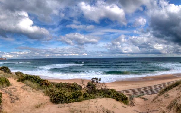 HD desktop wallpaper showing the natural beauty of Phillip Island with sandy dunes, ocean waves, and a dramatic cloudy sky on a scenic island coastline.