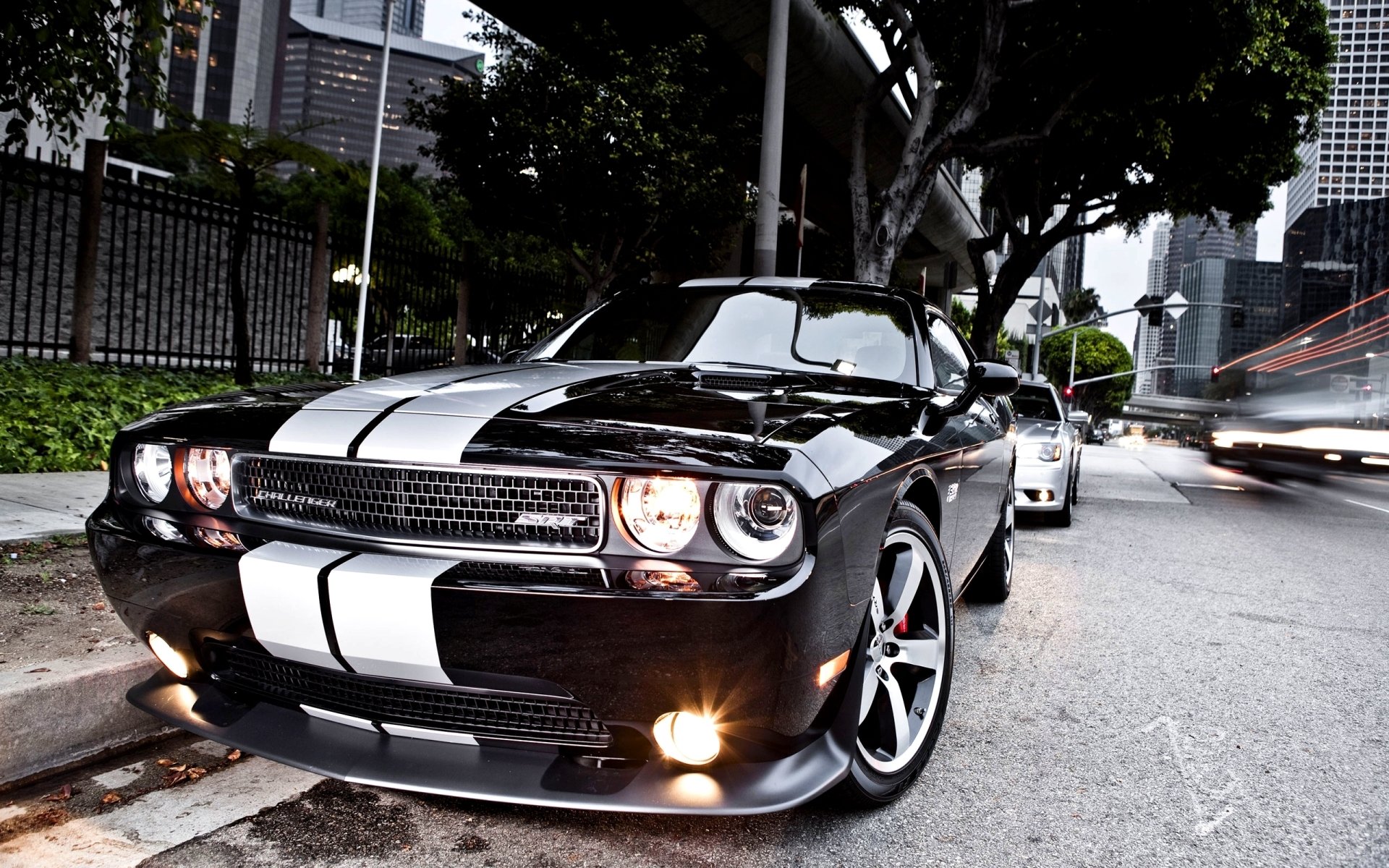 Black Dodge Challenger SRT8 with white racing stripes, front three-quarter view parked on a city street — 2K Quad HD PC desktop wallpaper/background.