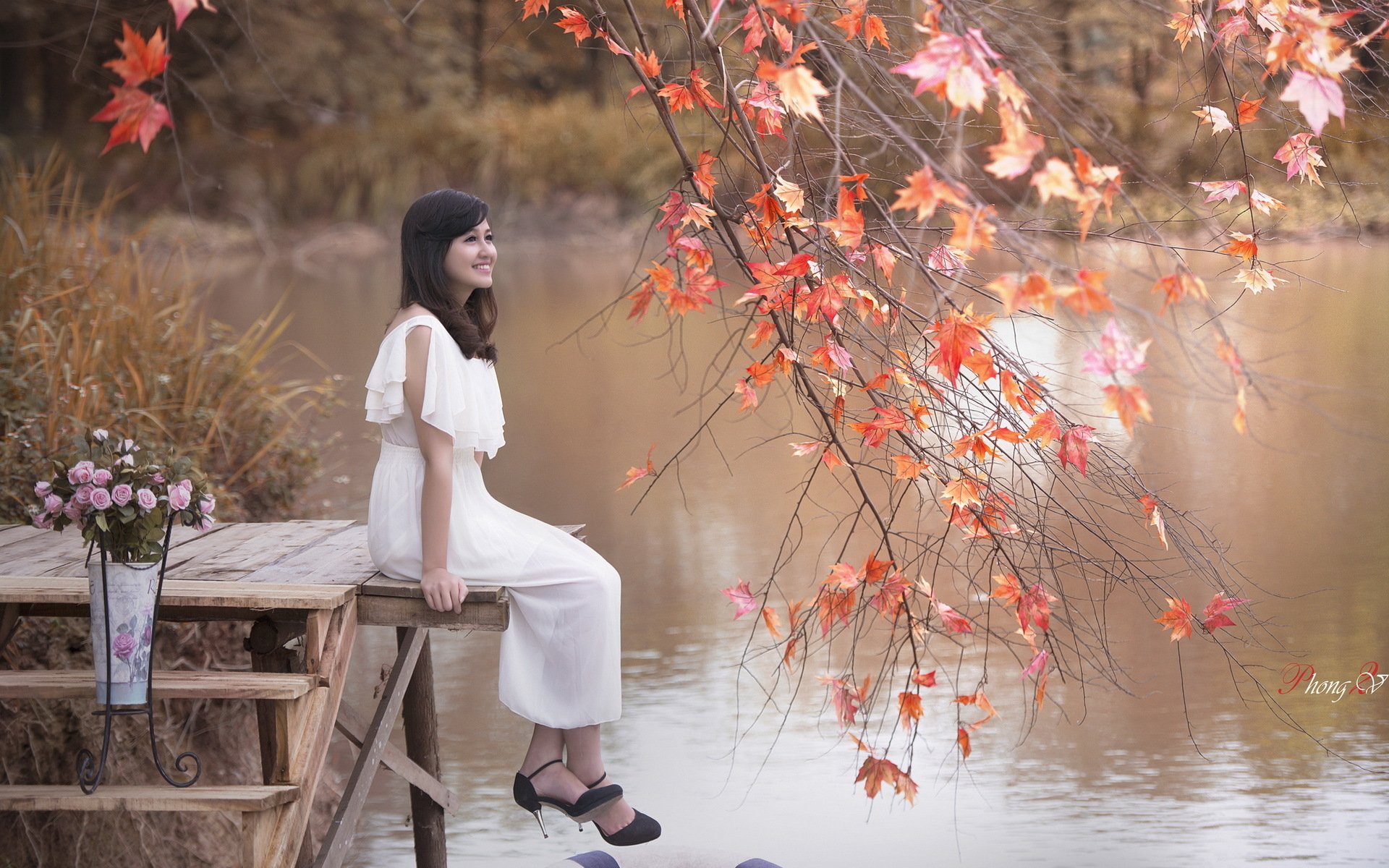 A serene scene featuring an Asian woman in a white dress sitting on a dock, surrounded by autumn leaves reflecting in a calm water body, creating a soothing HD desktop wallpaper.