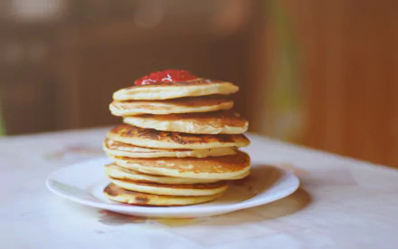 Syrup-drizzled stack of pancakes topped with a strawberry on a plate, warm blurred backdrop — 2K Quad HD PC desktop wallpaper and background. food, pancake