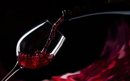 A close-up of red wine being poured into a glass, against a dark background, with vibrant swirls of color, creating an elegant and inviting food and wine-themed desktop wallpaper.