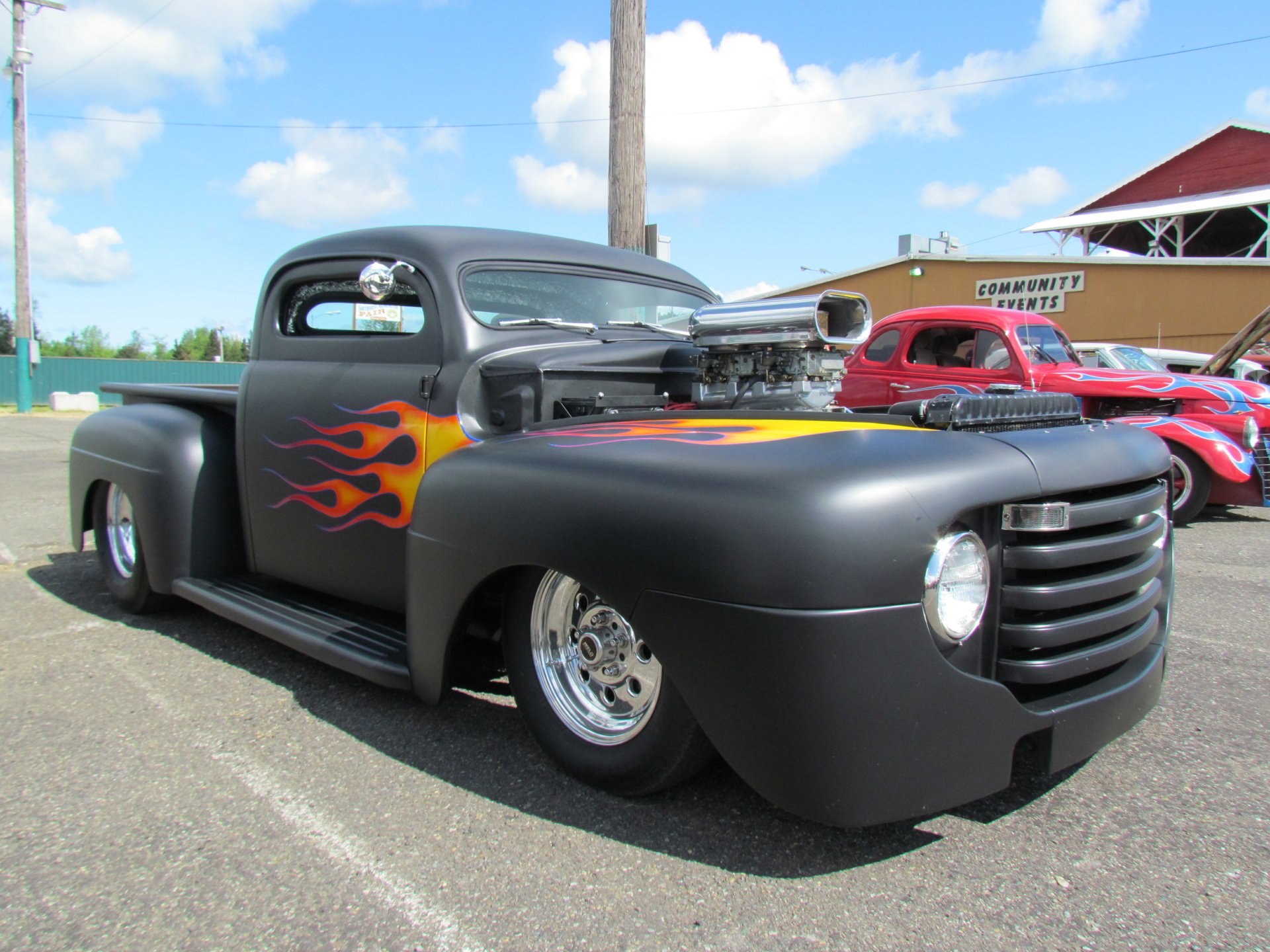Vintage Ford truck with matte black paint and flame decals, showcased in a clear outdoor setting, captured in 4K Ultra HD for PC desktop wallpaper use.
