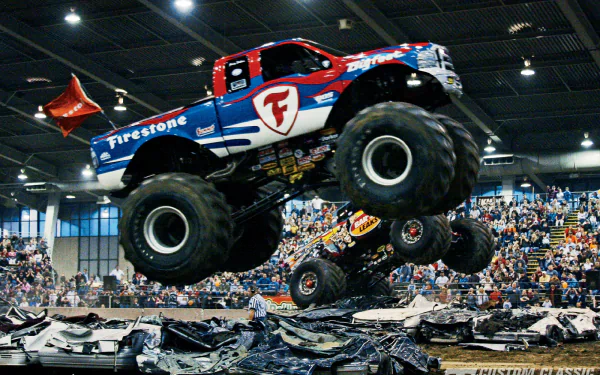 A vibrant image of a monster truck performing a jump over crushed cars, showcasing high energy at an indoor arena, serving as a dynamic HD PC desktop wallpaper and background.