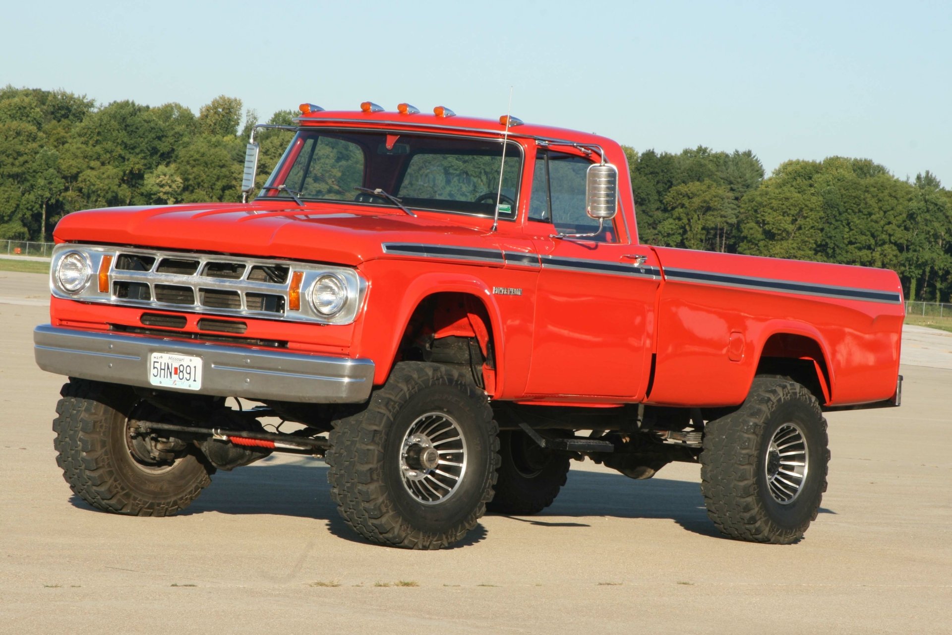 A vibrant red Dodge Power Wagon truck parked on a concrete surface with trees in the background, captured in 4K Ultra HD for PC desktop wallpaper.